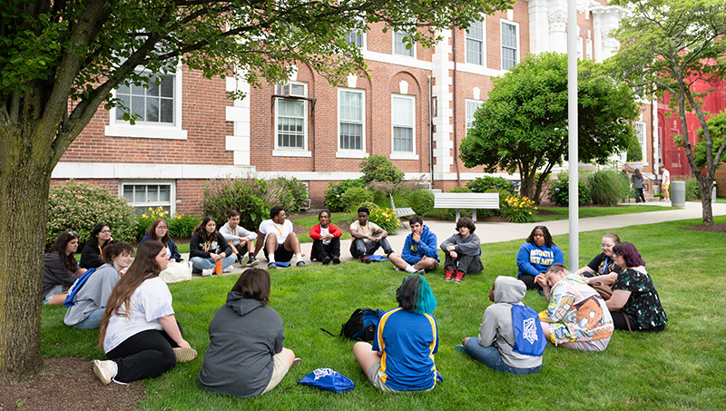 Students sitting in a circle, outside, on campus.