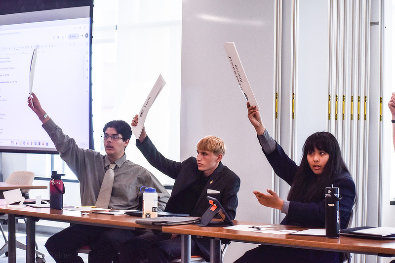 Students in a classroom all raising their hands.