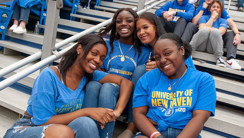 Four University of New Haven students pose for the camera in the stands during homecoming.