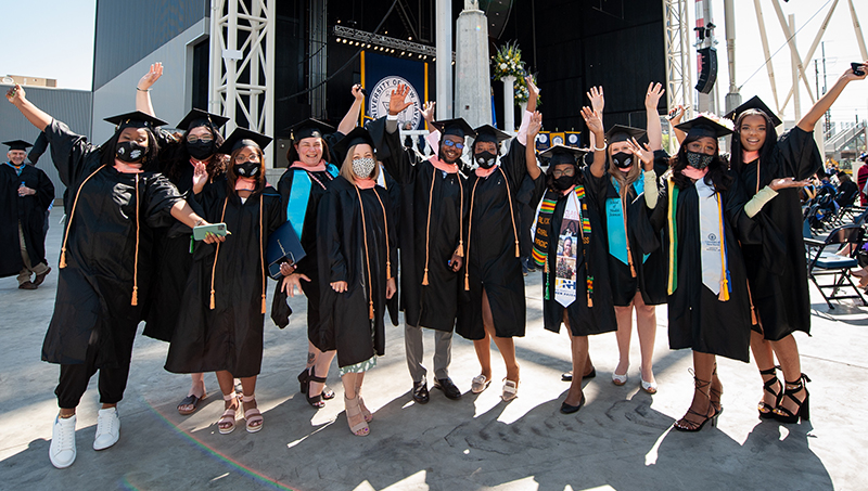 Students at commencement, posing for a photo and waving their hands in the air.