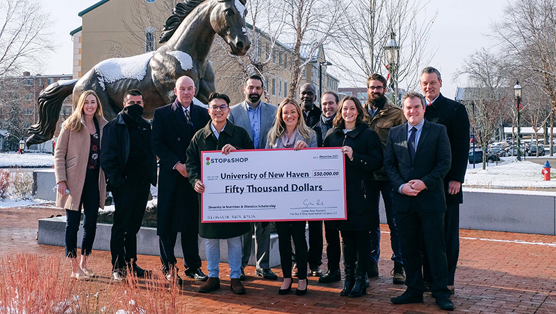 Representatives from Stop & Shop pose with University faculty and staff for a photo outside by a statue of a horse.